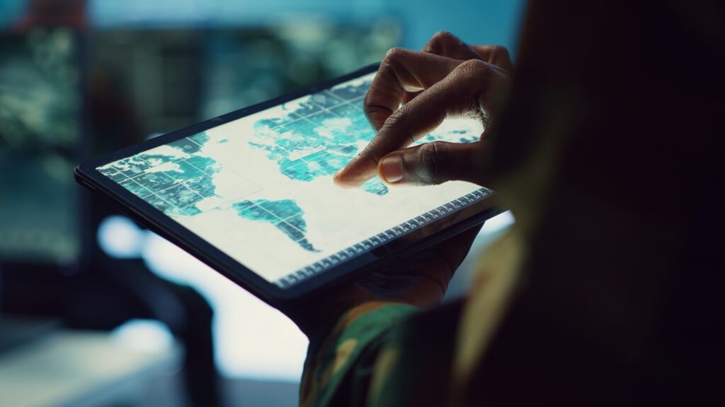 Military IT professional gathers intelligence from world map projection, tablet connected to satellite reconnaissance system to support field troops. Dispatch army command post. Close up. Camera A.